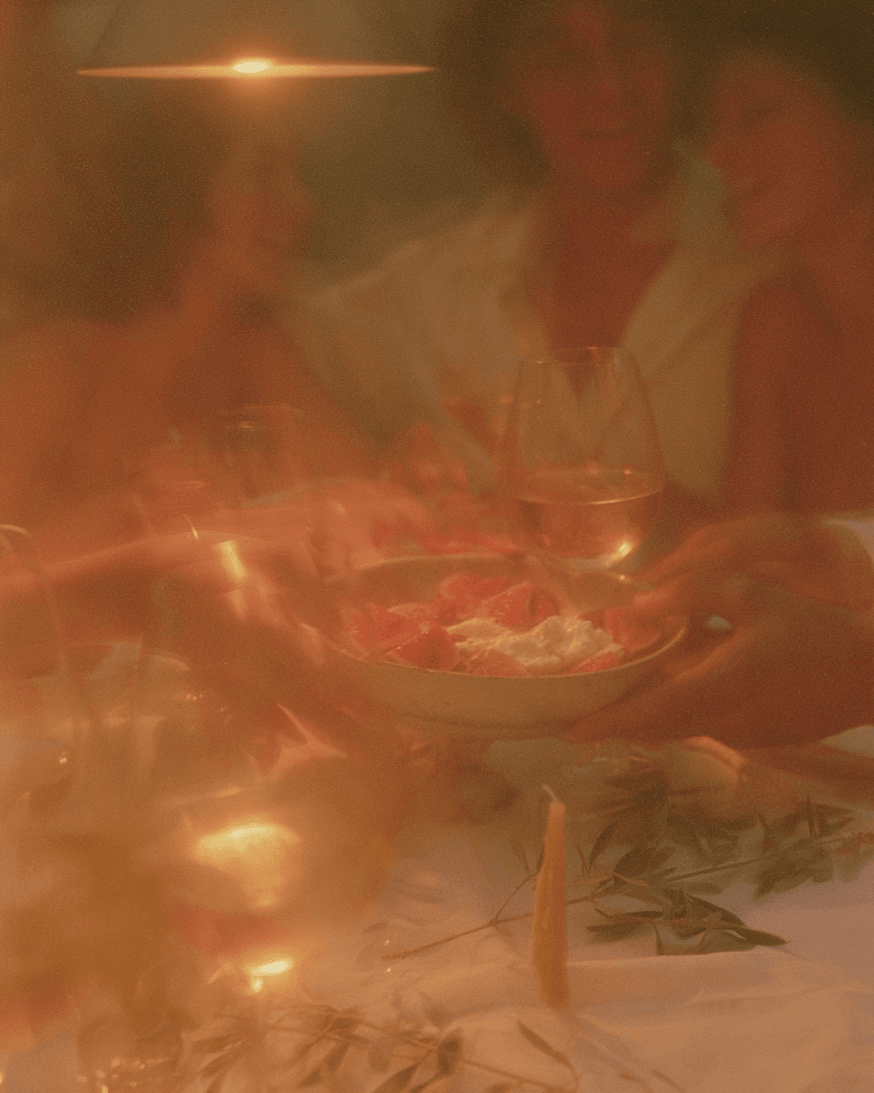 A candlelit dinner table at dusk with hands passing a dish, evoking the shared meals the Food Intolerance test helps untangle